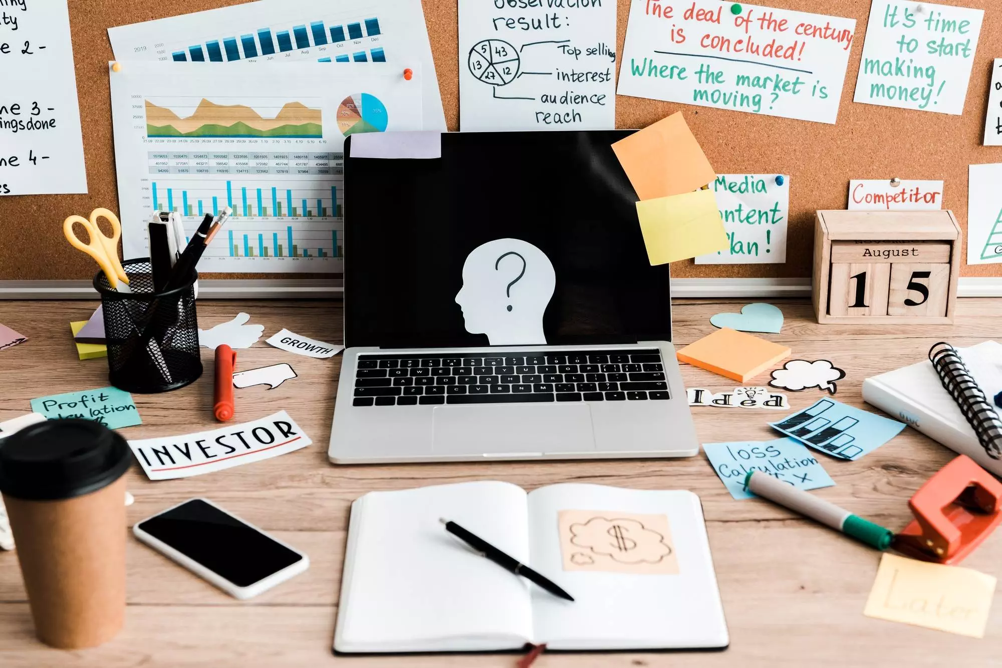 laptop and smartphone with blank screens on table near notice board with letters and sticky notes
